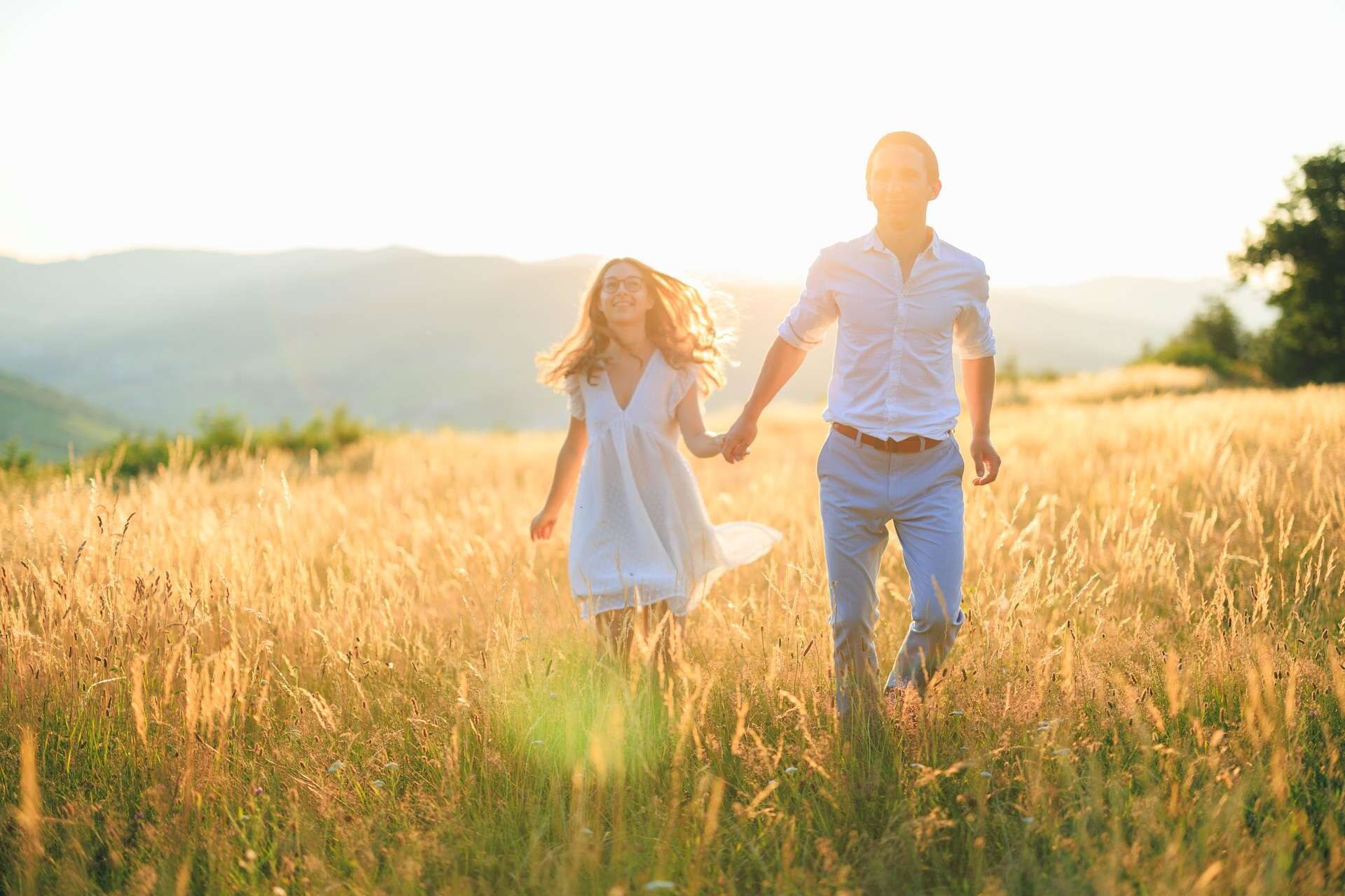 couple souriant courant dans un champ de blé au coucher du soleil